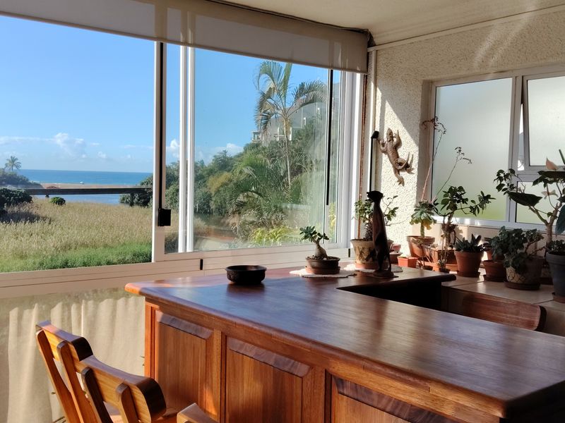 Enclosed balcony featuring a built-in wooden bar counter, large sliding glass doors, and expansive coastal views.
