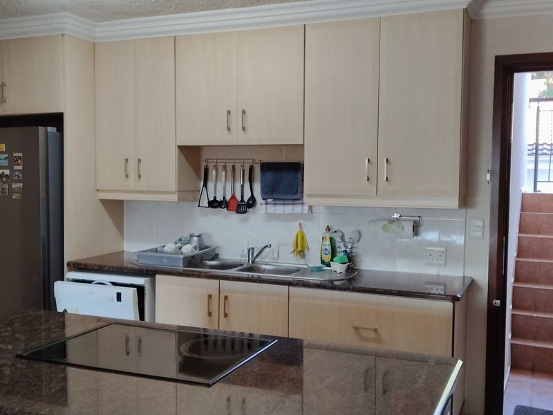 Functional kitchen featuring light wood-finish cabinetry, granite countertops, and a central island with a built-in hob, providing efficient workspace and storage.