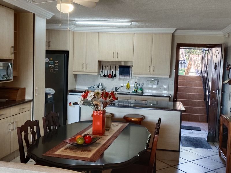 Open plan kitchen and dining area featuring light wood cabinetry, granite countertops, breakfast bar, and tiled flooring with direct access to an outdoor staircase.