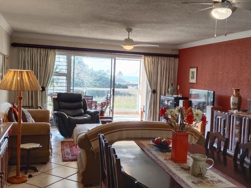 Spacious open-plan living and dining area featuring tiled floors, ceiling fans, and large sliding doors leading to an outdoor balcony with scenic views.