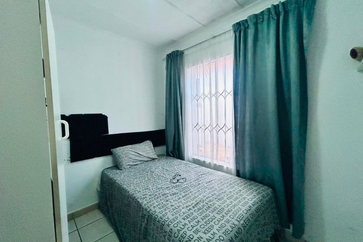 A standard bedroom featuring tiled flooring and a window fitted with security bars.