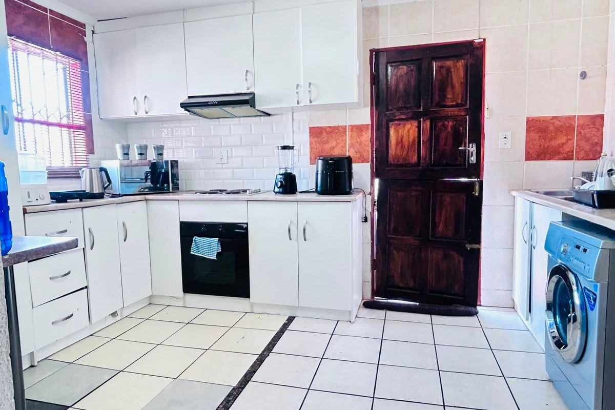 Functional kitchen featuring white cabinetry, built-in oven, extractor fan, tiled backsplash, and direct access to the exterior via a wooden door.