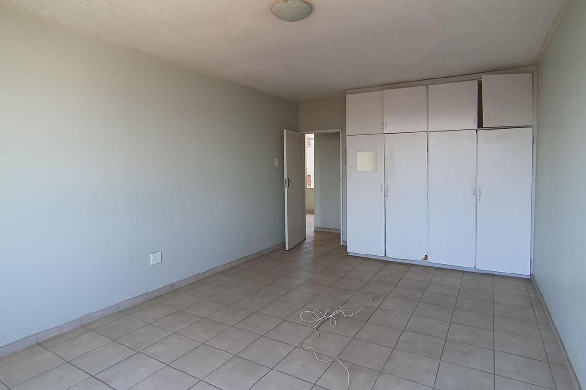 An empty bedroom featuring tiled flooring and built-in cupboards, offering a blank canvas for personalization.