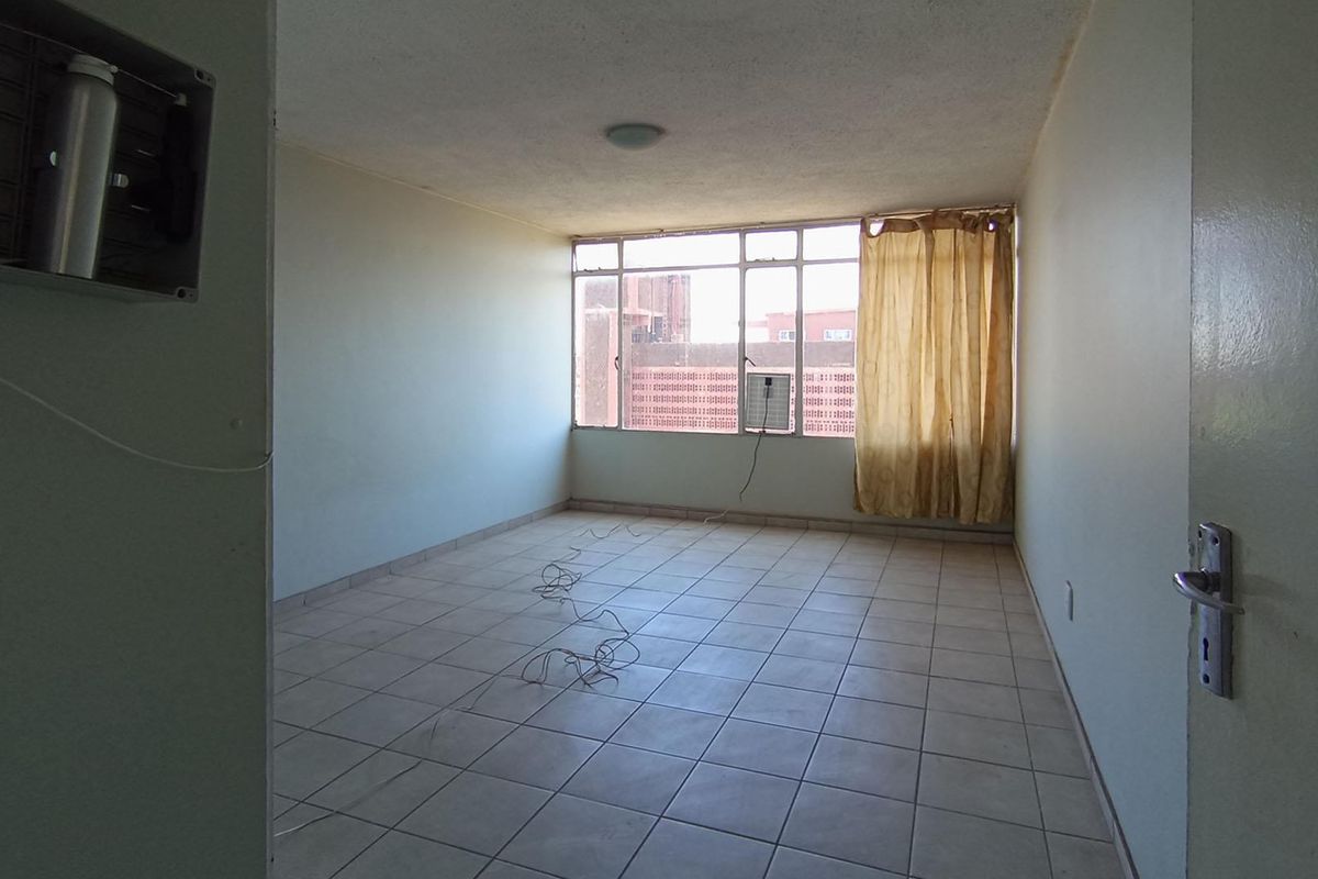 An empty living room featuring tiled flooring, a window-mounted air conditioning unit, and large windows providing natural light.