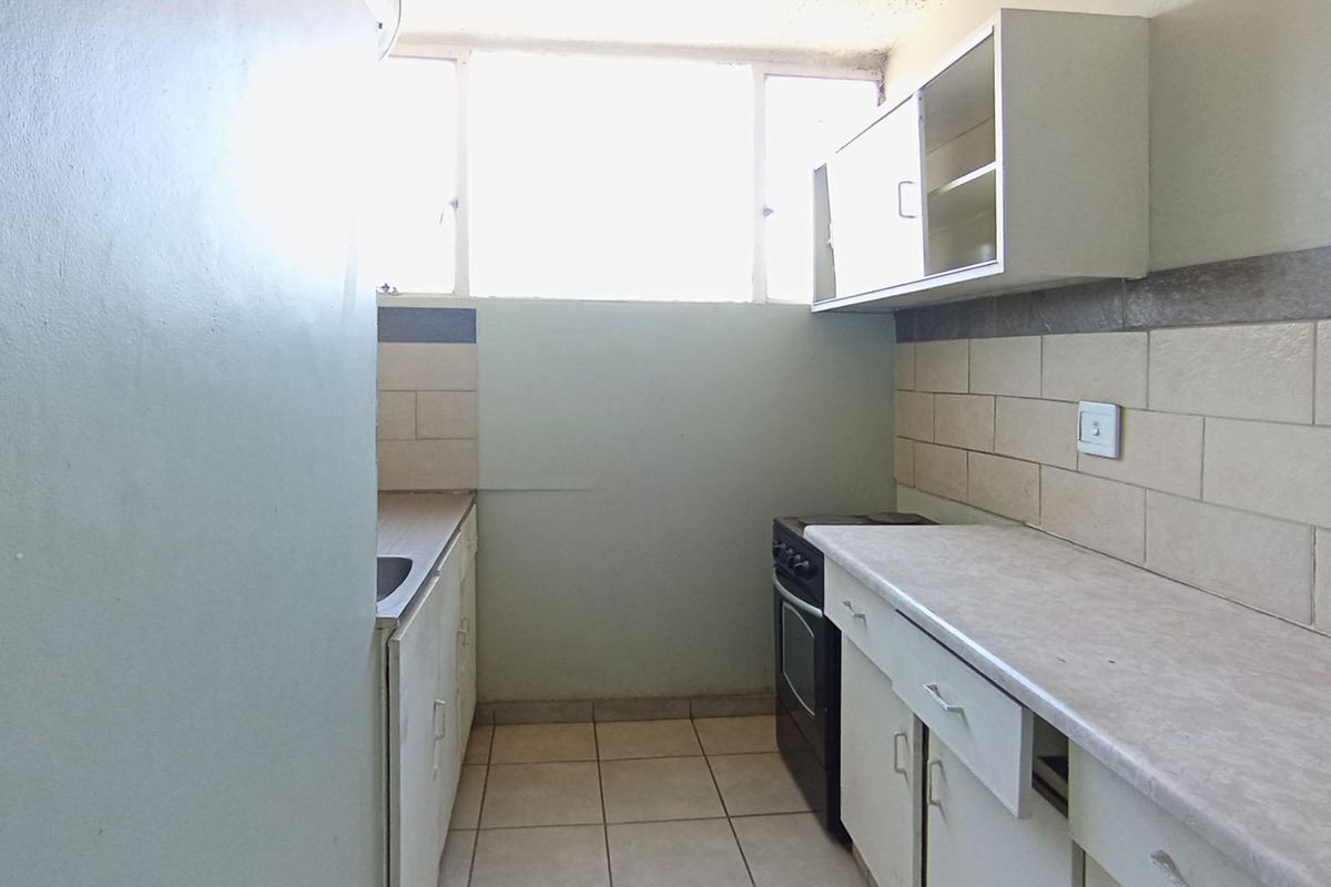 A compact, functional kitchen featuring built-in cabinetry, laminate countertops, a stainless steel sink, and a freestanding stove with tiled backsplash and flooring.