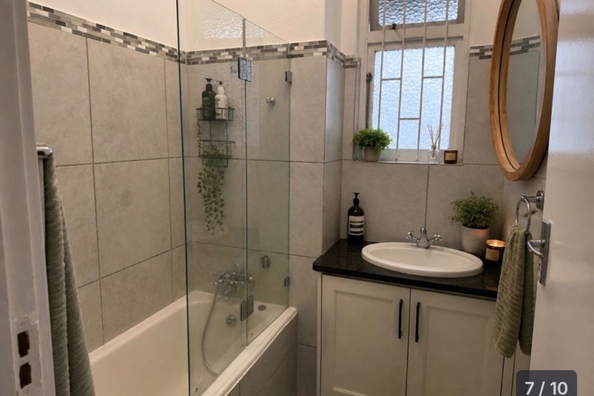 A well-maintained bathroom featuring a bathtub with a glass screen, a vanity cabinet with a granite countertop, and neutral wall tiling.