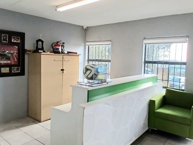 A functional industrial reception area featuring tiled flooring, security bars on windows, and a built-in reception desk.