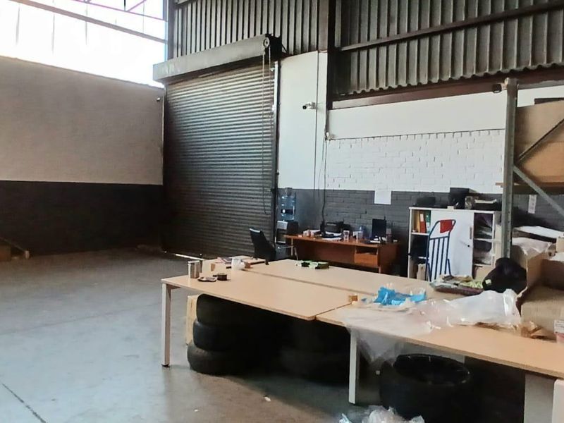 Spacious industrial warehouse area featuring high ceilings, exposed steel roof structure, concrete flooring, and a large roller shutter door for easy access.