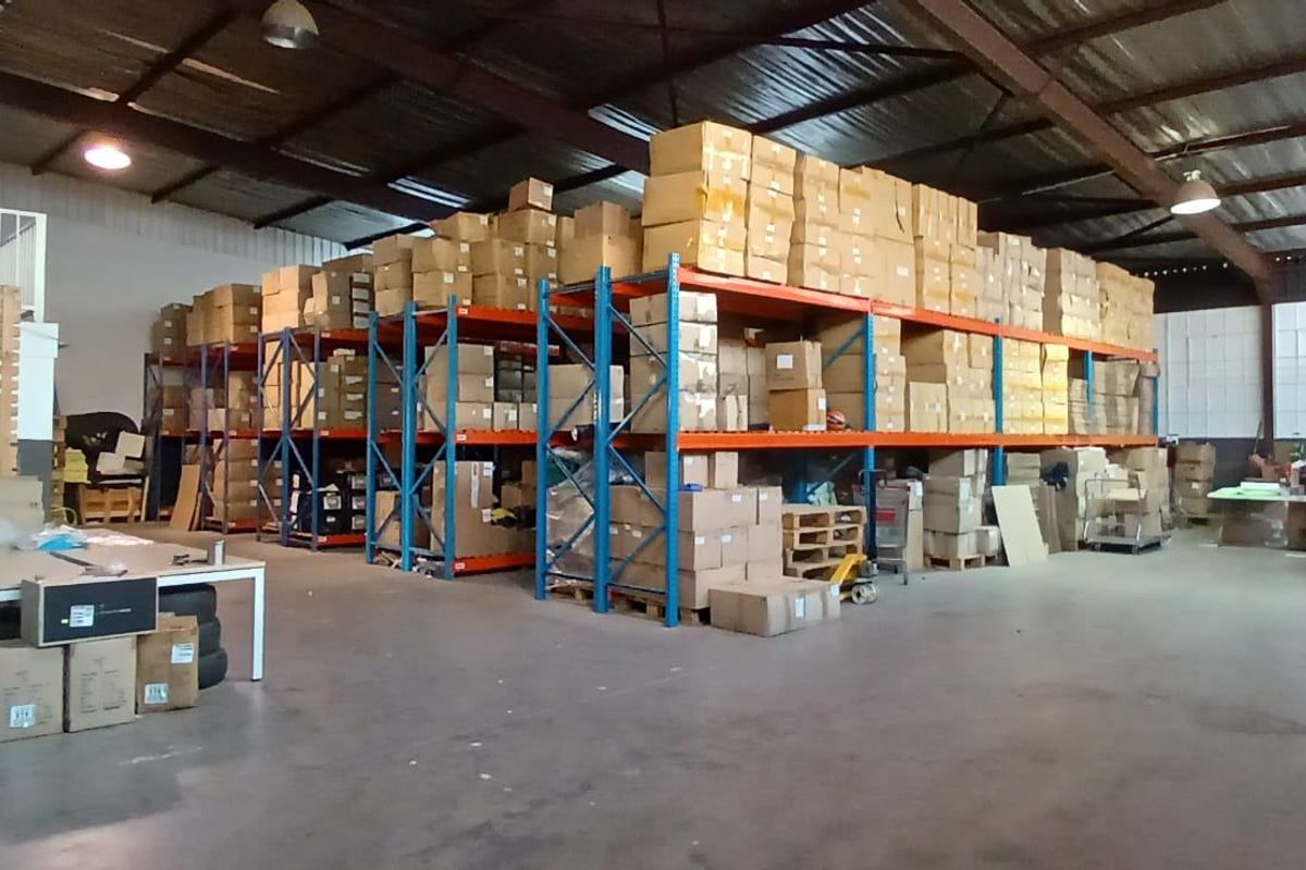 Spacious industrial warehouse featuring high ceilings with exposed steel trusses, concrete flooring, and extensive built-in steel racking systems for storage.