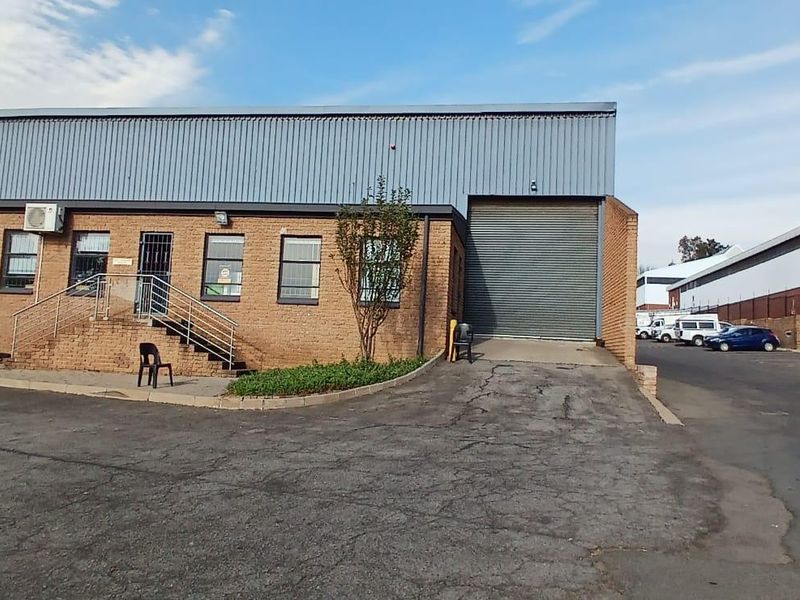Industrial property exterior featuring a brick facade, large roller shutter door, and asphalt driveway with adjacent water storage tanks.