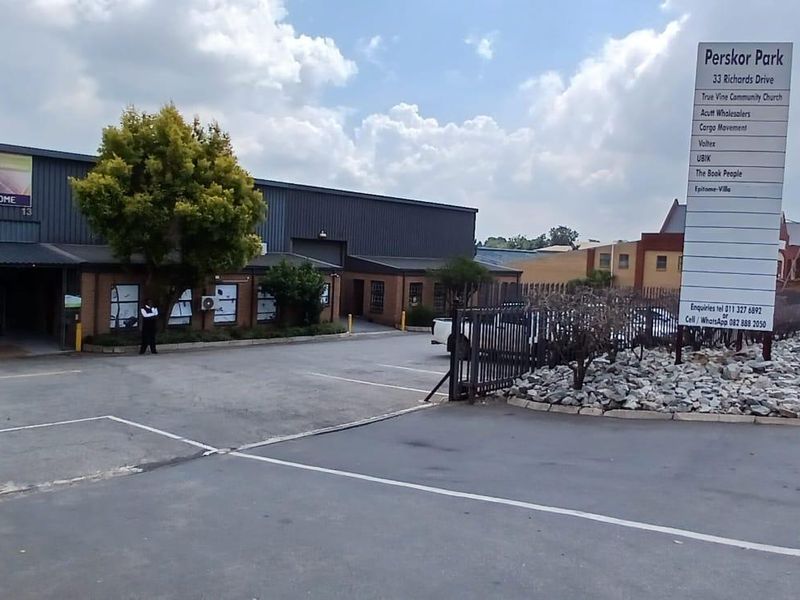 Front exterior view of Perskor Park industrial complex featuring a paved driveway, security gate, and prominent tenant signage.
