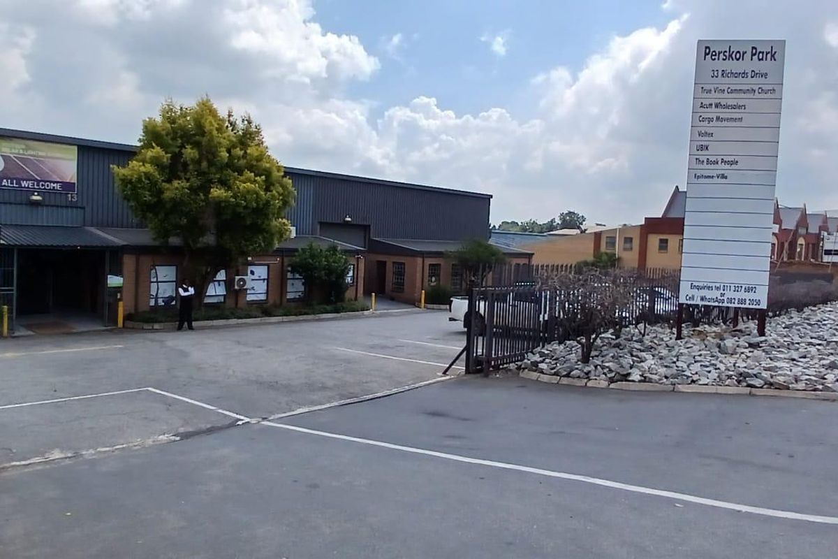 Front exterior view of Perskor Park industrial complex featuring a paved driveway, security gate, and prominent tenant signage.