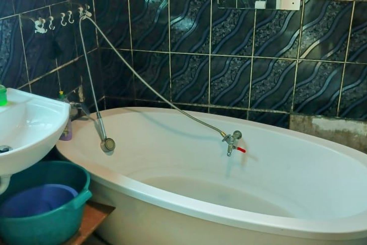 A compact bathroom featuring a pedestal basin and a freestanding bathtub with wall-mounted fixtures, finished with dark patterned ceramic wall tiles.