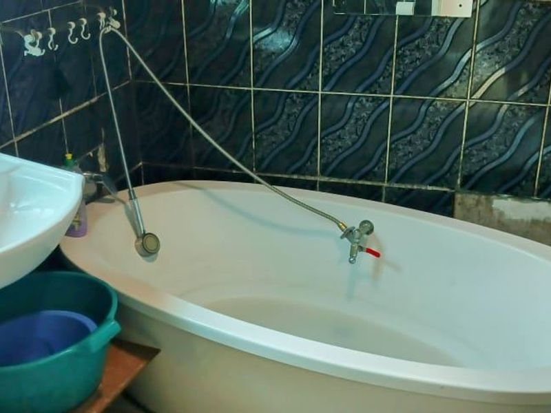 A compact bathroom featuring a pedestal basin and a freestanding bathtub with wall-mounted fixtures, finished with dark patterned ceramic wall tiles.