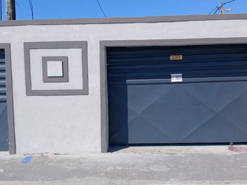 Front elevation of the property featuring a secure metal garage door and a matching pedestrian gate set within a plastered boundary wall.