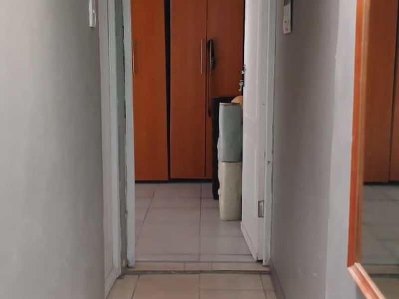 A narrow hallway with tiled flooring leading into a bedroom area featuring built-in wooden cupboards.