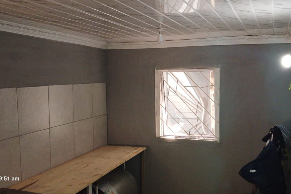 A functional kitchen area featuring a tiled splashback, security burglar bars on the window, and PVC ceiling panels with decorative coving.