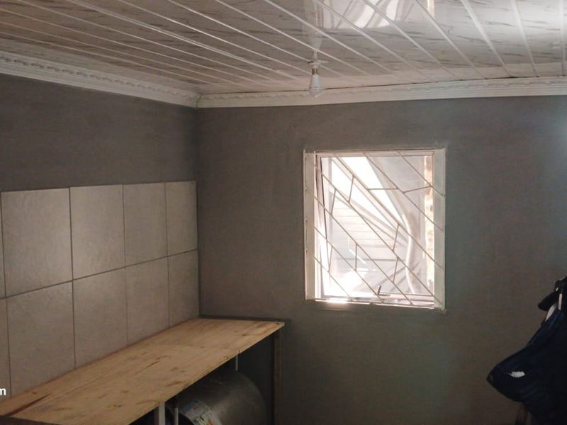 A functional kitchen area featuring a tiled splashback, security burglar bars on the window, and PVC ceiling panels with decorative coving.