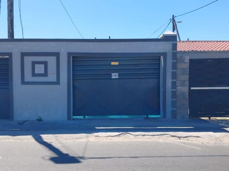 Front elevation of the property featuring a secure perimeter wall, metal garage door, and gated pedestrian and vehicle access.
