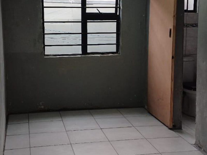 An empty bedroom featuring tiled flooring, security bars on the window, and a sliding door leading to an adjacent bathroom area.