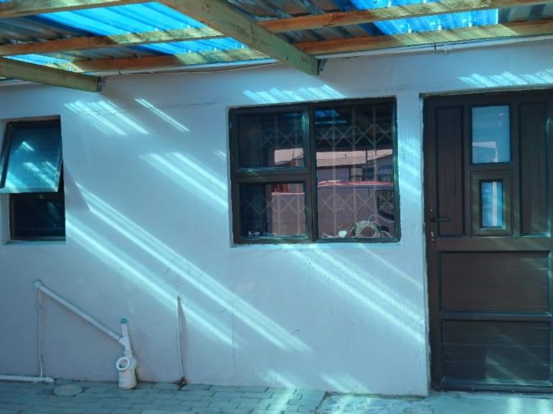 A covered outdoor patio area featuring a timber-framed corrugated roof, paved flooring, and direct access to the home via a secure door.
