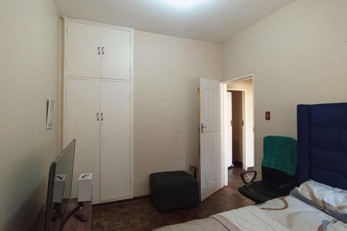 A bedroom featuring parquet flooring and a built-in wardrobe, offering a functional space with potential for cosmetic updates.