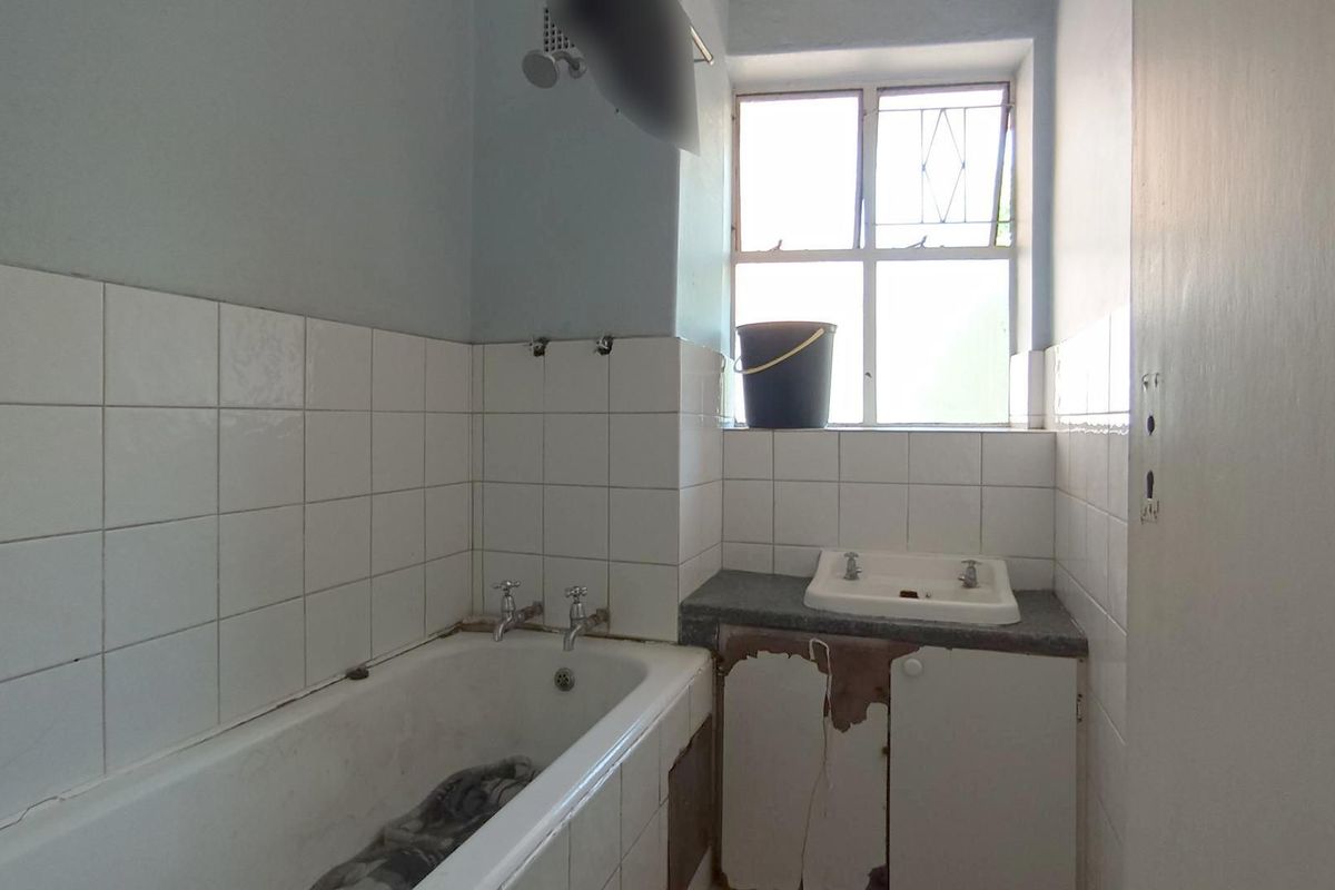 A dated bathroom featuring a standard bathtub and vanity basin, requiring renovation to address damaged cabinetry and worn finishes.