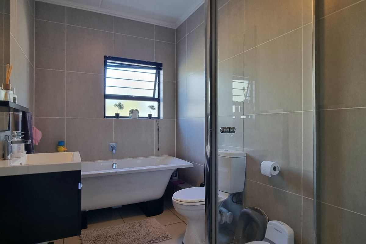 Modern bathroom featuring a freestanding bathtub, glass-enclosed shower, wall-mounted vanity, and neutral floor-to-ceiling tiling.