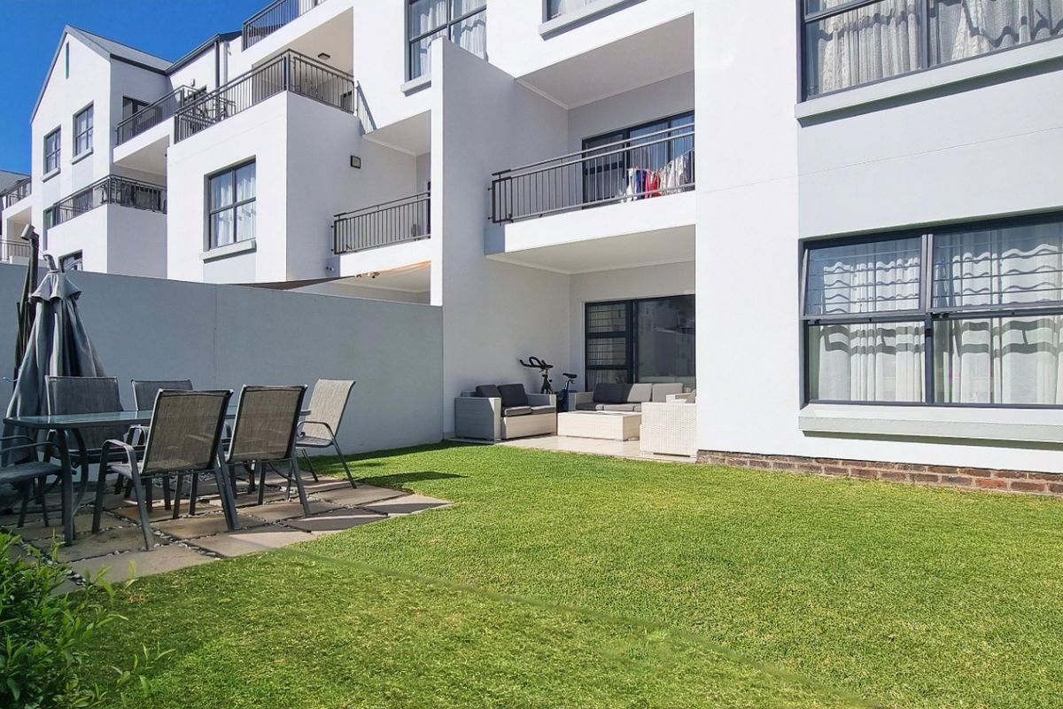 A well-maintained ground floor apartment featuring a private garden, paved patio area, and access to an upper-level balcony.