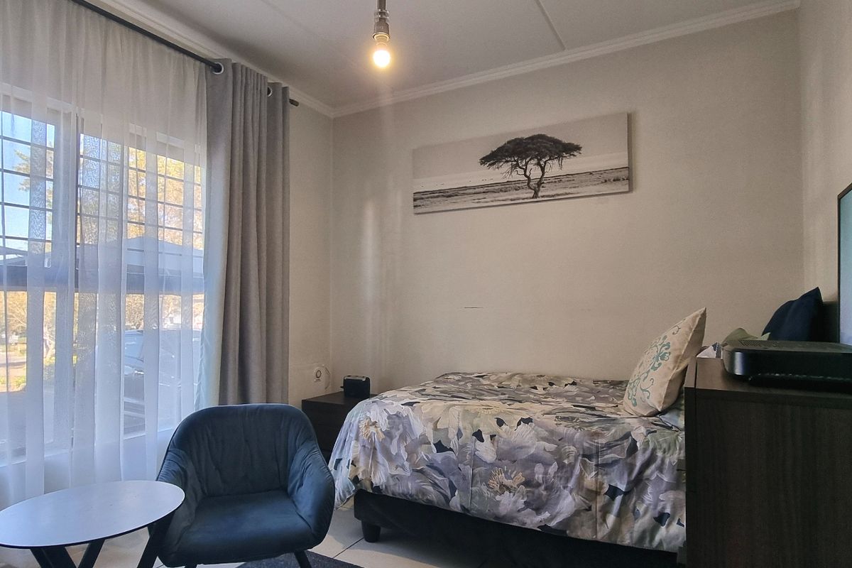 A functional bedroom featuring tiled flooring, large windows with security bars, and neutral wall finishes, providing a comfortable living space.