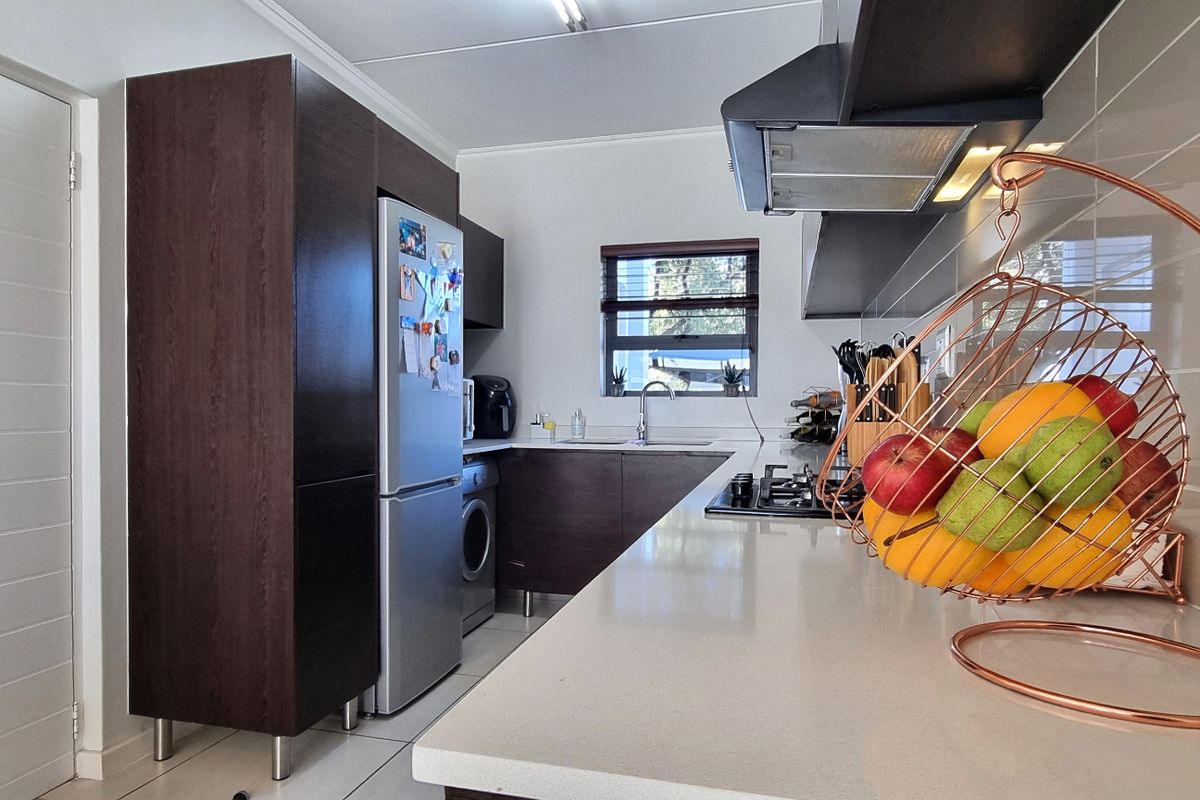 A functional kitchen featuring dark wood cabinetry, stone countertops, a gas hob with extractor fan, and tiled finishes throughout.
