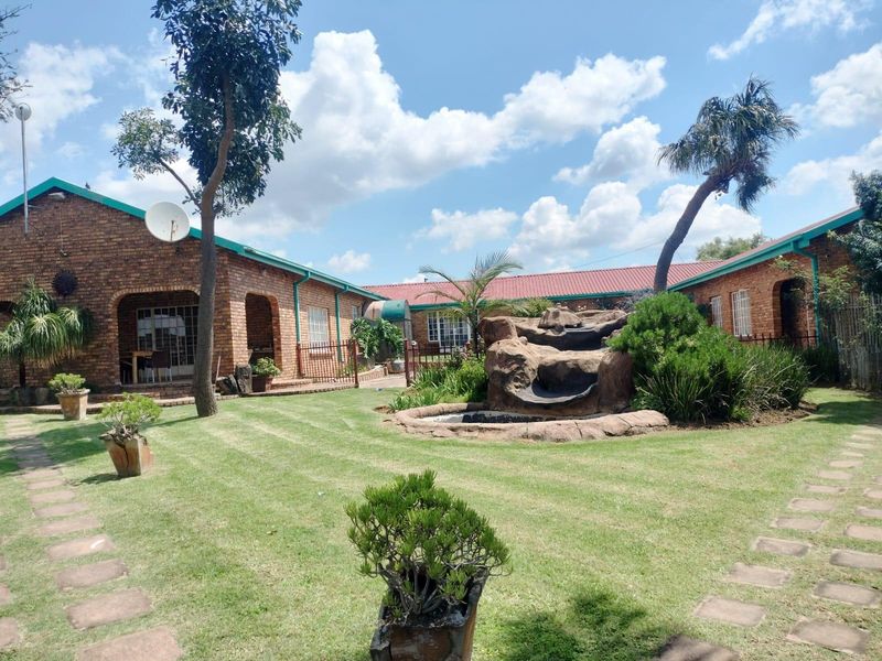 Spacious rear garden featuring a face brick house with a covered patio and a decorative rock water feature.