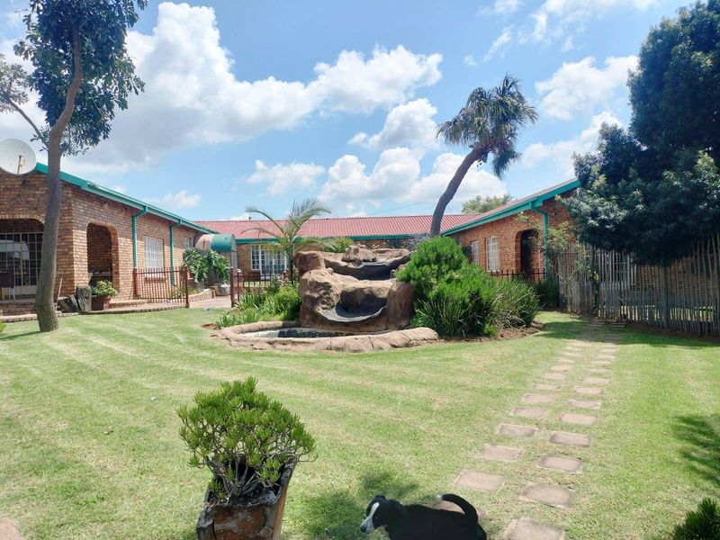 A spacious rear garden featuring a central stone water feature, manicured lawn, and paved pathway, surrounded by a brick-built residential structure.