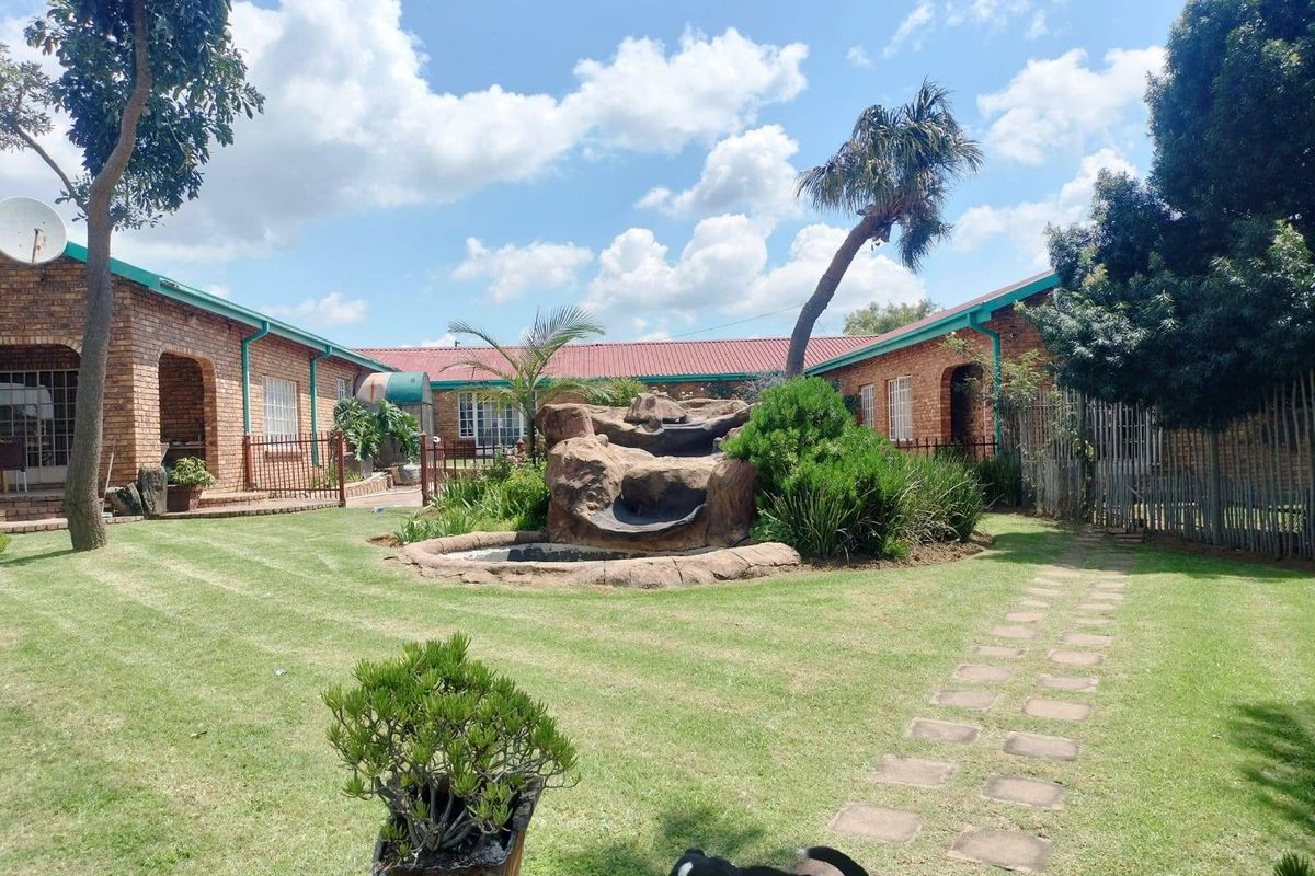 A spacious rear garden featuring a central stone water feature, manicured lawn, and paved pathway, surrounded by a brick-built residential structure.