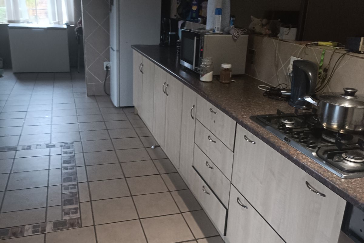 A functional kitchen featuring laminate cabinetry, dark countertops, a gas hob, and tiled flooring, offering a practical layout with potential for modern updates.