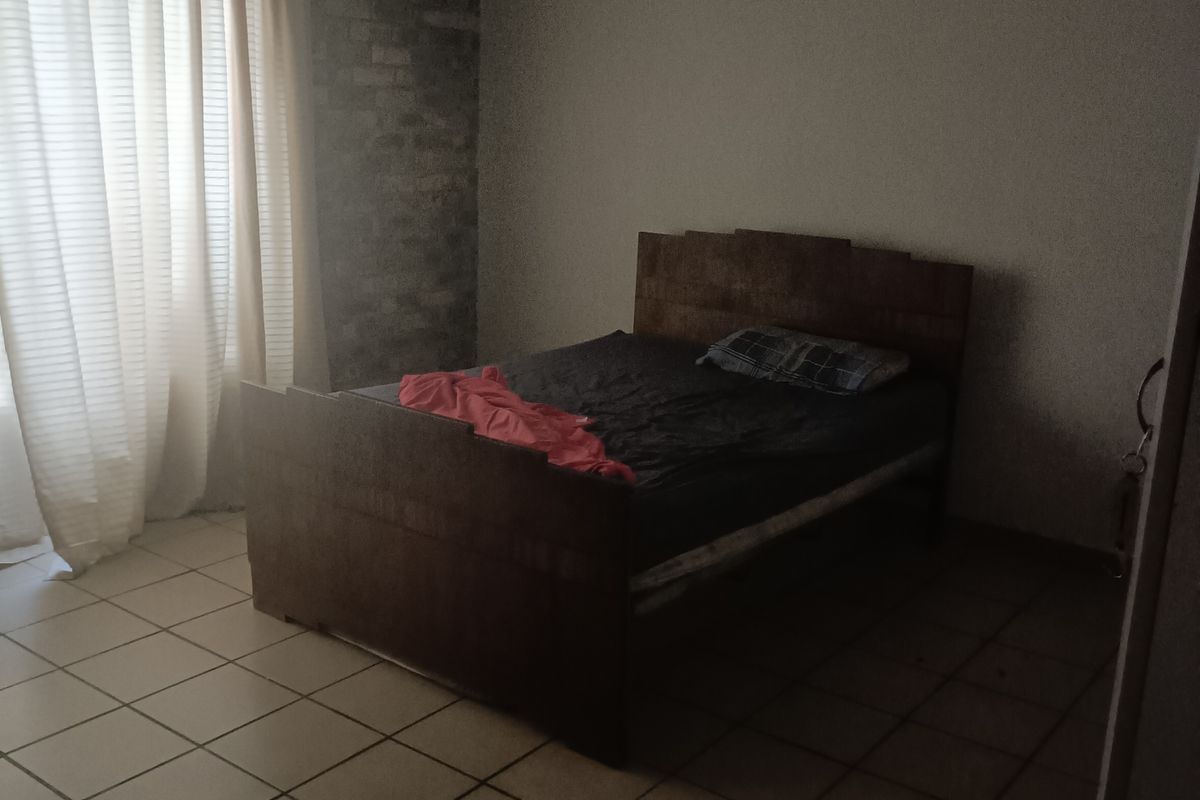 A bedroom featuring ceramic floor tiles, an exposed brick feature wall, and a ceiling fan, requiring cosmetic updates to improve the overall aesthetic.