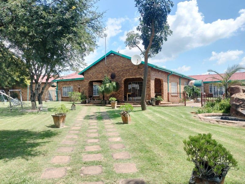 A spacious rear garden featuring a face brick house with a covered patio, stone walkway, and established landscaping.