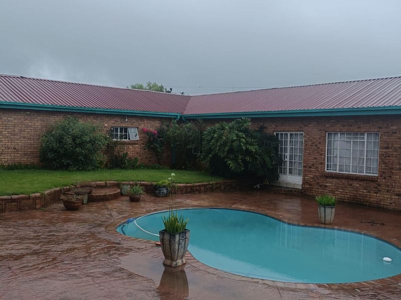 Rear exterior view featuring a swimming pool, stamped concrete patio, and brick house facade with a metal roof.