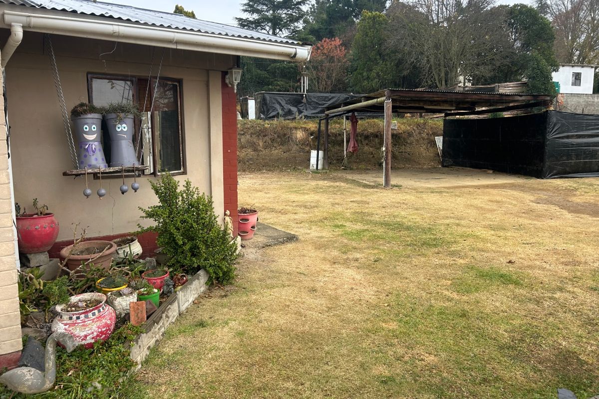 Rear exterior view of the property featuring a lawn area, a basic carport structure, and the side elevation of the main dwelling.