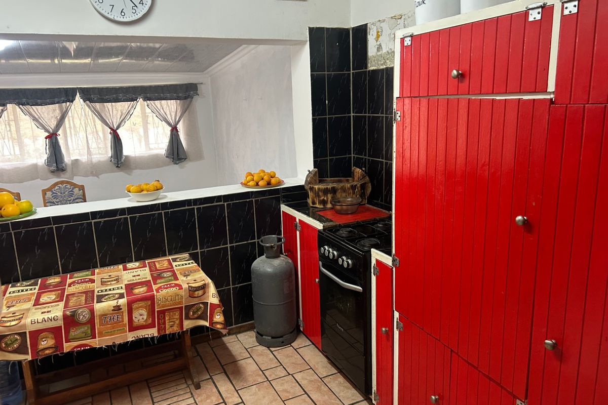 A dated kitchen featuring red cabinetry, black tiled splashbacks, and a gas stove, offering potential for a modern renovation.