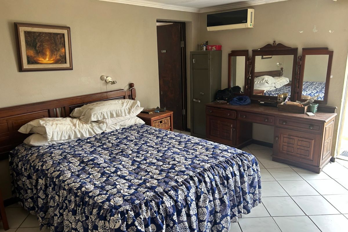 A bedroom featuring tiled flooring, coving, and a wall-mounted air conditioning unit, showing signs of wear on the walls and ceiling.