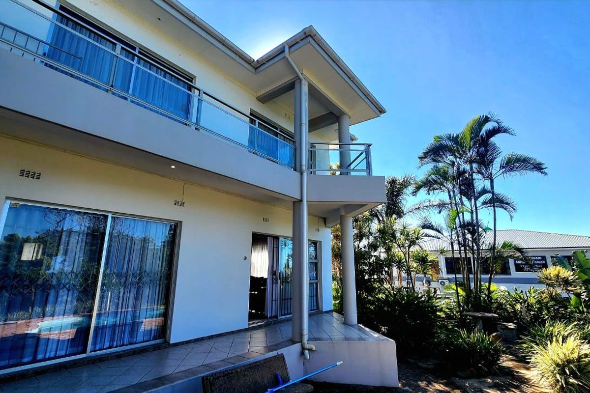 Rear view of a two-story commercial building featuring a tiled patio, upper-level balcony with glass balustrades, and sliding door access.