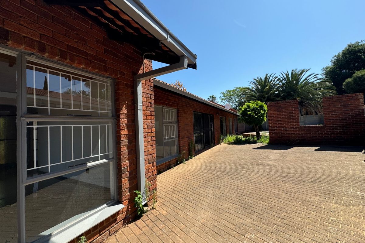 Rear exterior view of the property featuring a red brick facade, tiled roof, and a spacious paved patio area.