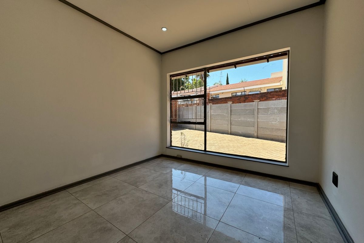 A bright, empty bedroom featuring neutral tiled flooring, recessed downlighting, and a large window overlooking the rear exterior area.