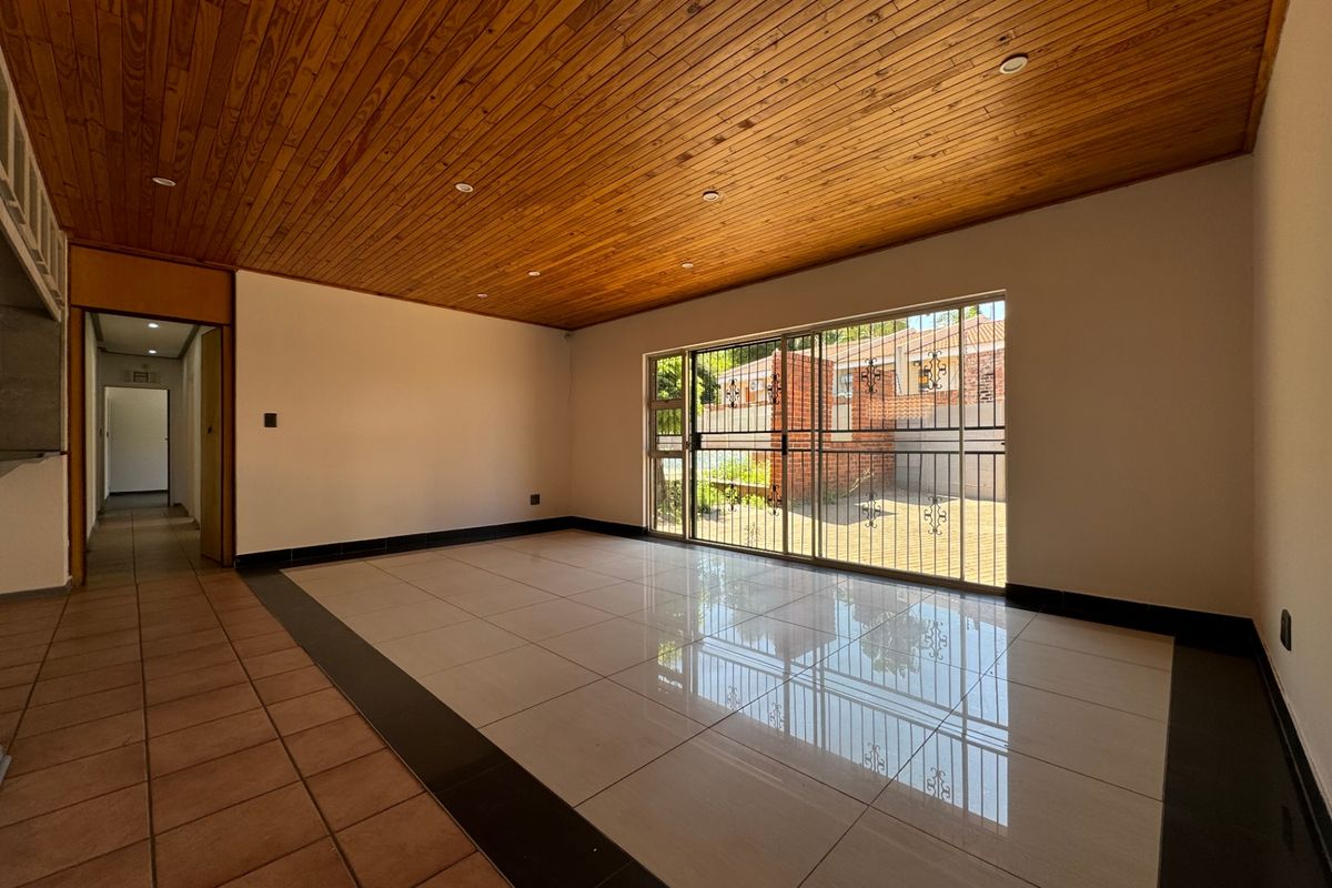 Spacious living area featuring a warm timber ceiling, polished porcelain floor tiles, and large sliding glass doors providing access to the rear exterior.