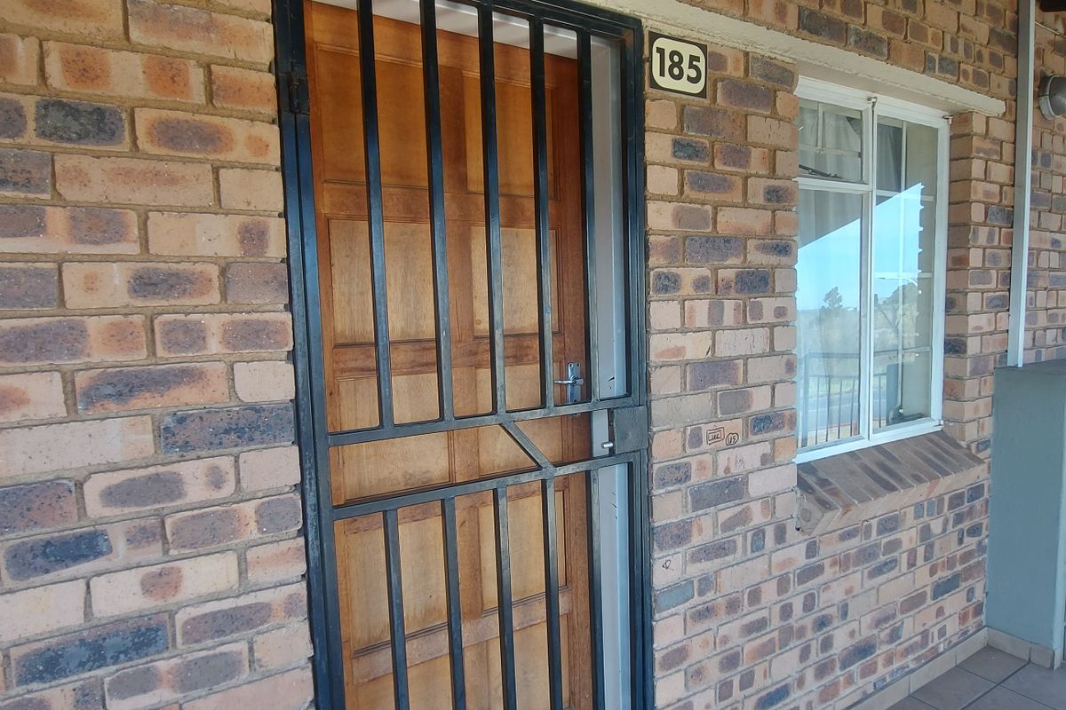 Front entrance of a townhouse featuring a face brick facade, secure metal gate, and timber door with adjacent window.