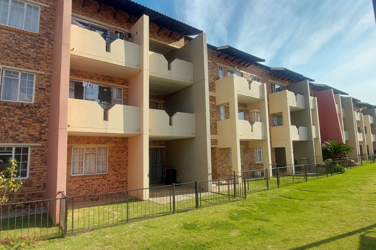 Rear elevation of a multi-story townhouse complex featuring face brick construction, private balconies, and a shared lawn area with perimeter fencing.