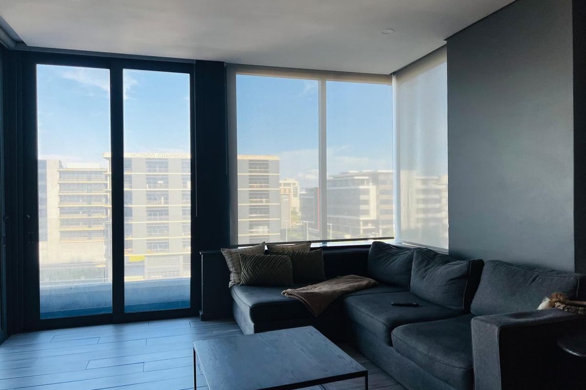 Modern living room featuring large floor-to-ceiling windows, sleek dark tiled flooring, recessed lighting, and access to an outdoor area.