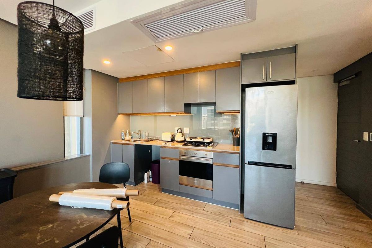 Modern kitchen featuring grey cabinetry, integrated oven, gas hob, glass splashback, and wood-look tile flooring in an open-plan layout.