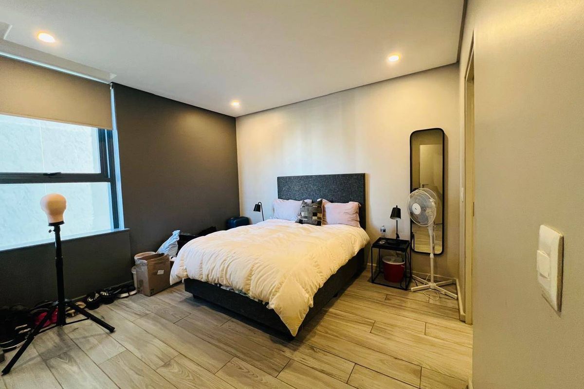 A well-maintained bedroom featuring modern wood-look tile flooring, recessed downlighting, and a large window with roller blinds.